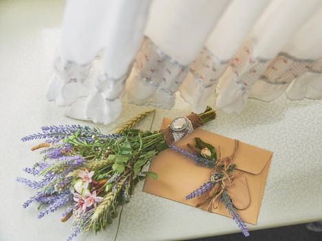 bridal bouquet of lavender in a boho style lies on the window near the handmade envelope, on top of the wedding dress