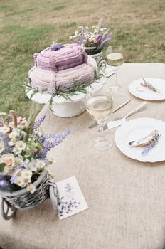 boho style wedding cake on a table covered with a linen tablecloth, with plates, glasses, knife fork and a bouquet of flowers