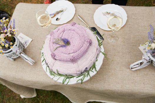 boho style wedding cake on a table covered with a linen tablecloth, with plates, glasses, knife fork and a bouquet of flowers