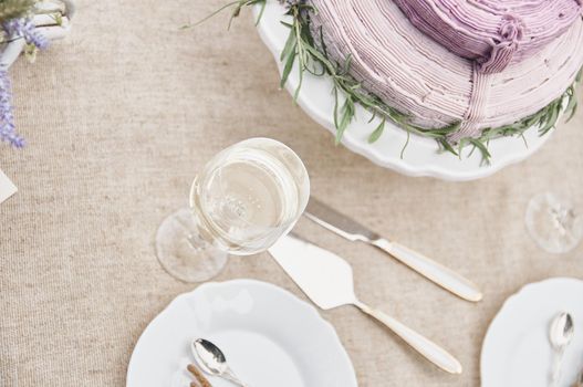 boho style wedding cake on a table covered with a linen tablecloth, with plates, glasses, knife fork and a bouquet of flowers