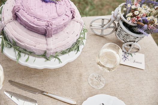 boho style wedding cake on a table covered with a linen tablecloth, with plates, glasses, knife fork and a bouquet of flowers