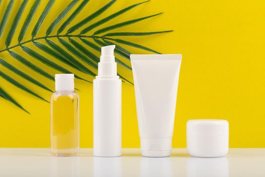 Set of cosmetic products on white table against yellow background with palm leaf. Concept of organic cosmetics with natural ingredients or skin care during summer
