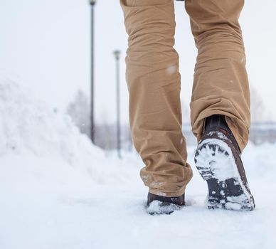 A person is walking on a slippery road, the first snow in the park, winter shoes, the road is covered with slippery ice and white snow. Footprints and shoes close-up.