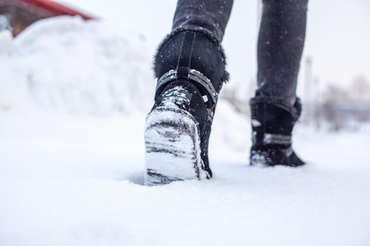 A person is walking on a slippery road, the first snow in the park, winter shoes, the road is covered with slippery ice and white snow. Footprints and shoes close-up.