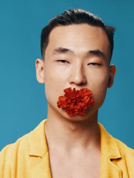 Portrait of a Korean man with a flower in his mouth on a blue background. High quality photo