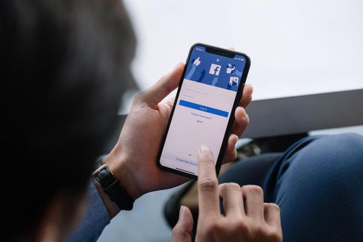 CHIANG MAI, THAILAND - JAN 17, 2021: Facebook social media app logo on log-in, sign-up registration page on mobile app screen on iPhone X in person's hand working on e-commerce shopping business