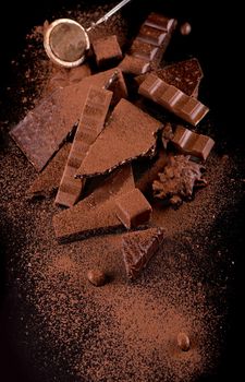 Broken chocolate pieces and cocoa powder on wooden background