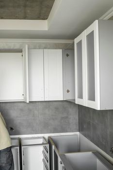 Custom kitchen cabinets installation with a white furniture facades mdf. Gray modular kitchen from chipboard material on a various stages of installation. A frame furniture fronts mdf profile