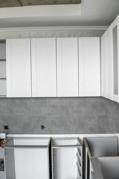 Custom kitchen cabinets installation with a white furniture facades mdf. Gray modular kitchen from chipboard material on a various stages of installation. A frame furniture fronts mdf profile