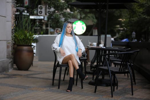 Happy stylish young hipster woman with long blue hair pink jacket, hat on the street in urban city.