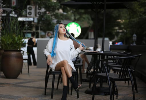 Happy stylish young hipster woman with long blue hair pink jacket, hat on the street in urban city.