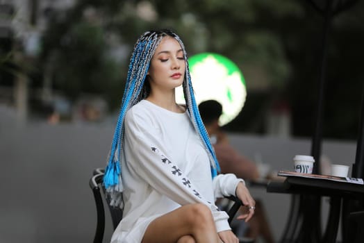 Happy stylish young hipster woman with long blue hair pink jacket, hat on the street in urban city.