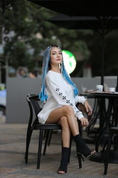 Happy stylish young hipster woman with long blue hair pink jacket, hat on the street in urban city.