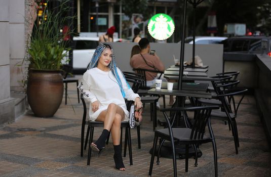 Happy stylish young hipster woman with long blue hair pink jacket, hat on the street in urban city.