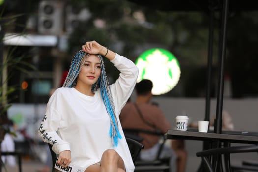 Happy stylish young hipster woman with long blue hair pink jacket, hat on the street in urban city.