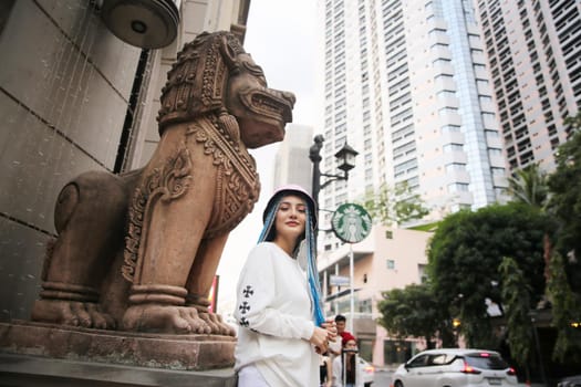 Happy stylish young hipster woman with long blue hair pink jacket, hat on the street in urban city.