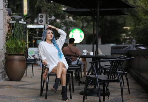 Happy stylish young hipster woman with long blue hair pink jacket, hat on the street in urban city.