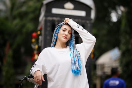 Happy stylish young hipster woman with long blue hair pink jacket, hat on the street in urban city.