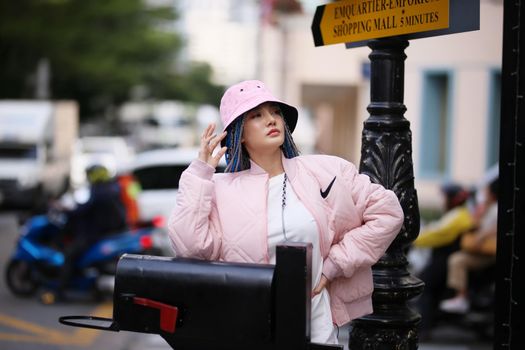 Happy stylish young hipster woman with long blue hair pink jacket, hat on the street in urban city.