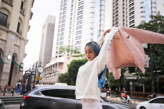 Happy stylish young hipster woman with long blue hair pink jacket, hat on the street in urban city.