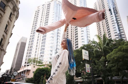 Happy stylish young hipster woman with long blue hair pink jacket, hat on the street in urban city.