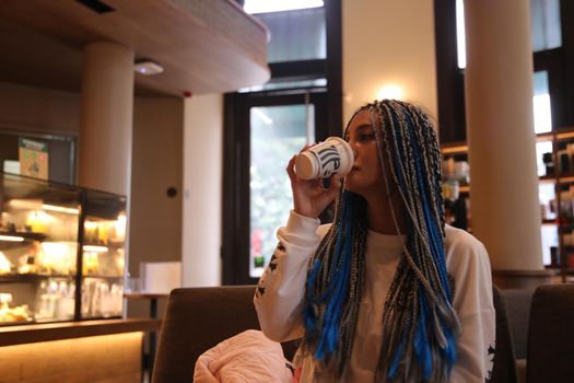 Happy stylish young hipster woman with long blue hair pink jacket, hat on the street in urban city.