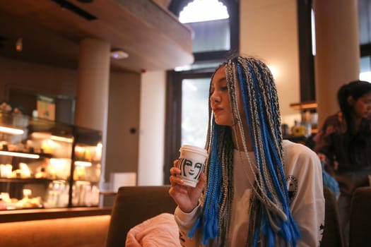 Happy stylish young hipster woman with long blue hair pink jacket, hat on the street in urban city.