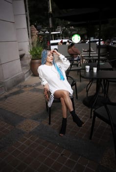 Happy stylish young hipster woman with long blue hair pink jacket, hat on the street in urban city.