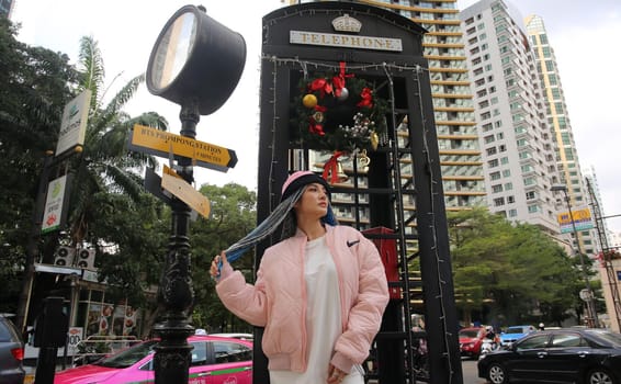 Happy stylish young hipster woman with long blue hair pink jacket, hat on the street in urban city.