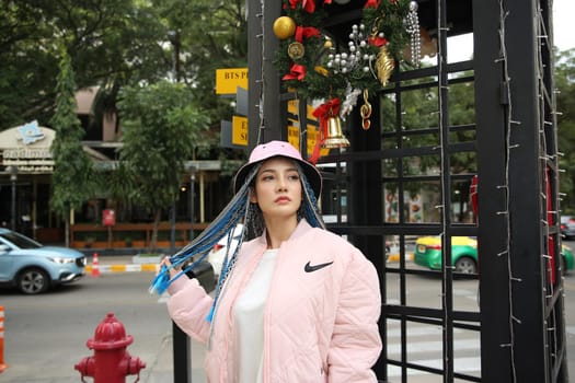 Happy stylish young hipster woman with long blue hair pink jacket, hat on the street in urban city.