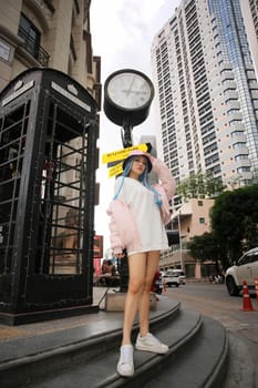 Happy stylish young hipster woman with long blue hair pink jacket, hat on the street in urban city.