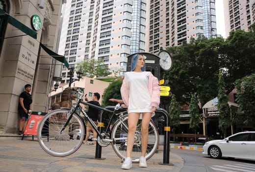 Happy stylish young hipster woman with long blue hair pink jacket, hat on the street in urban city.