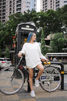 Happy stylish young hipster woman with long blue hair pink jacket, hat on the street in urban city.