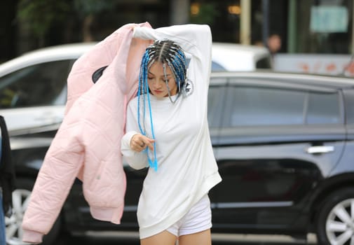 Happy stylish young hipster woman with long blue hair pink jacket, hat on the street in urban city.