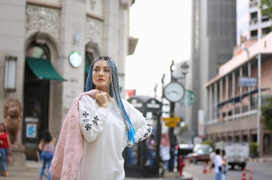 Happy stylish young hipster woman with long blue hair pink jacket, hat on the street in urban city.