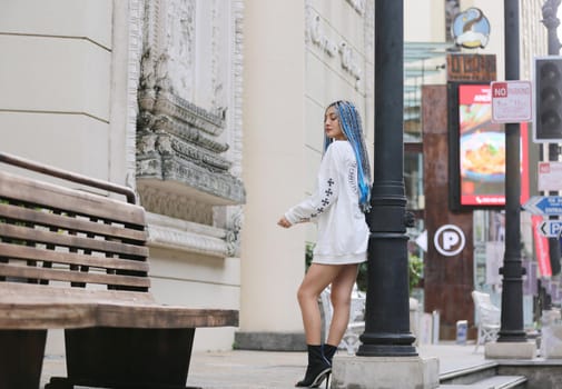 Happy stylish young hipster woman with long blue hair pink jacket, hat on the street in urban city.