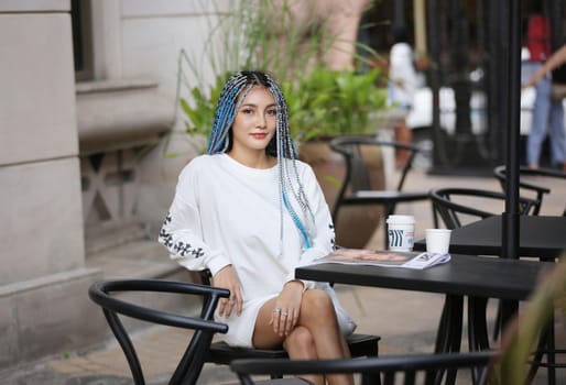 Happy stylish young hipster woman with long blue hair pink jacket, hat on the street in urban city.