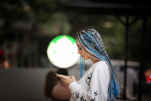 Happy stylish young hipster woman with long blue hair pink jacket, hat on the street in urban city.