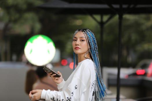 Happy stylish young hipster woman with long blue hair pink jacket, hat on the street in urban city.