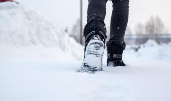 A person is walking on a slippery road, the first snow in the park, winter shoes, the road is covered with slippery ice and white snow. Footprints and shoes close-up.