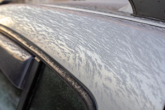 thin ice frost on silver car surface at morning - close-up with selective focus.