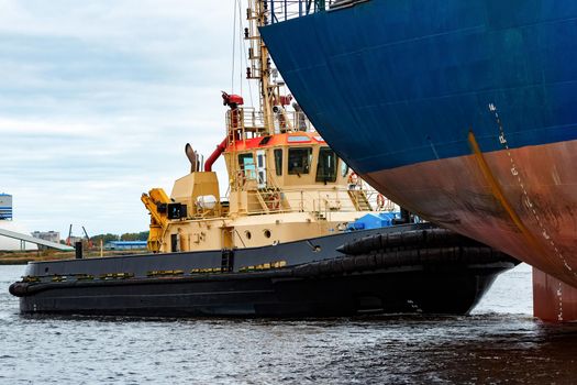 Tug ship towing blue bulk carrier in the port of Riga