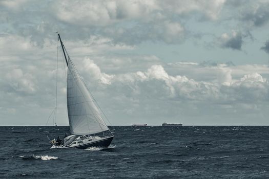 Blue sailboat in a travel at stormy sea. Regata journey. Toned