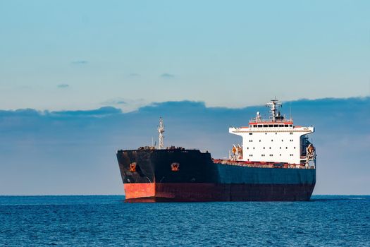 Black cargo ship moving in still Baltic sea water. Riga, Europe