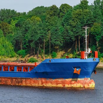 Blue cargo ship with long reach excavator moving to the port