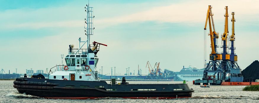 Black tug ship moving to the cargo terminal. Industrial service