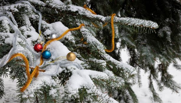 Christmas tree branch in the snow with toys and tinsel . Snow spruce branch in the forest. Russian winter landscape. Space for your text. Christmas composition.