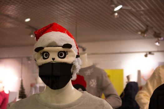 A mannequin in a Santa Claus hat wearing a black protective mask and a cute sleep mask.