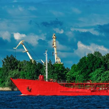 Red cargo tanker ship moving by the river