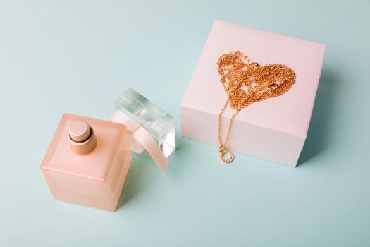 A gift for Valentine's Day. Perfume and a box with a gold chain on a blue background. Chain in the shape of a heart.